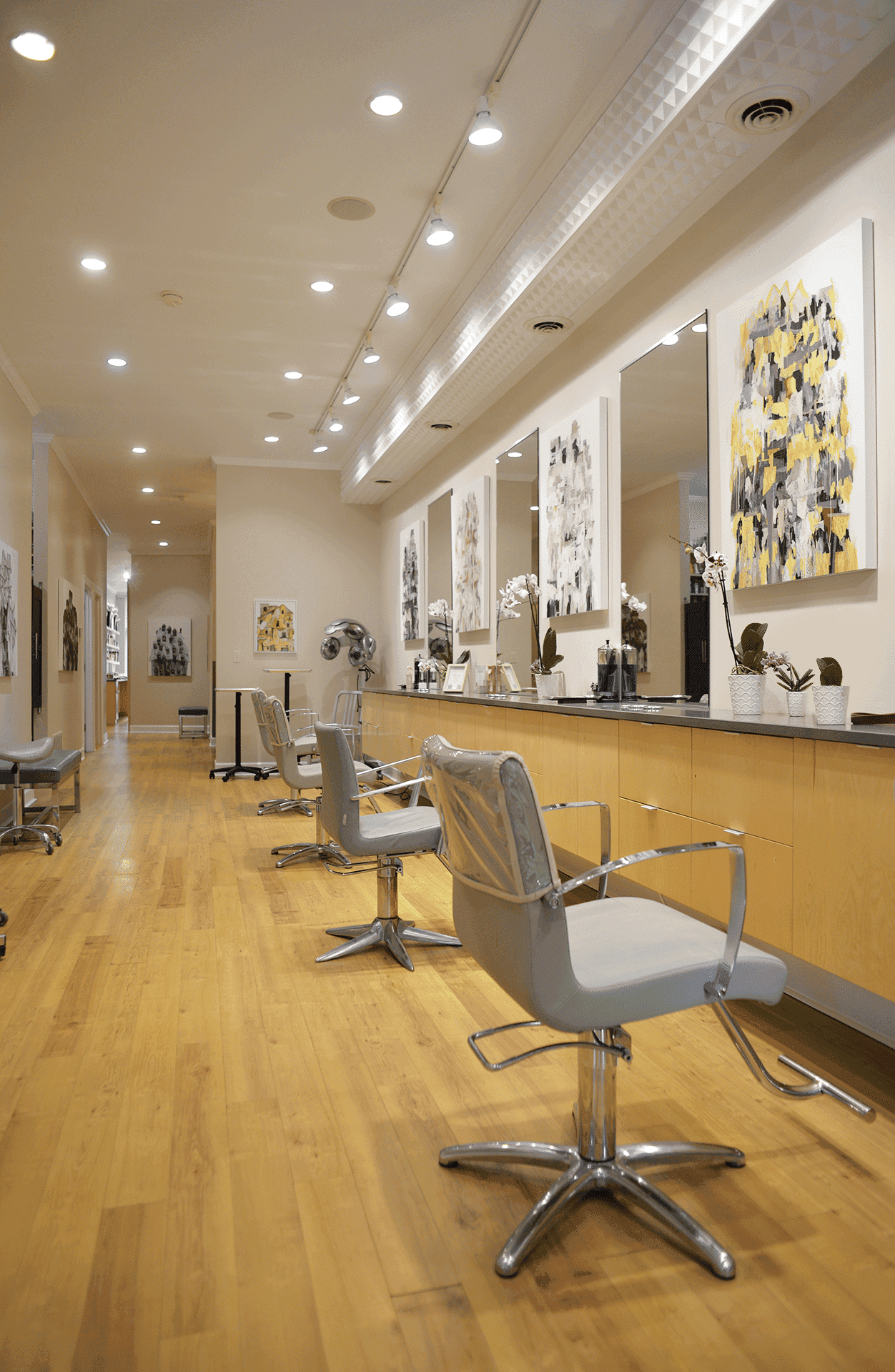 Modern hair salon interior with wooden floors, sleek chairs, and abstract art on walls.
