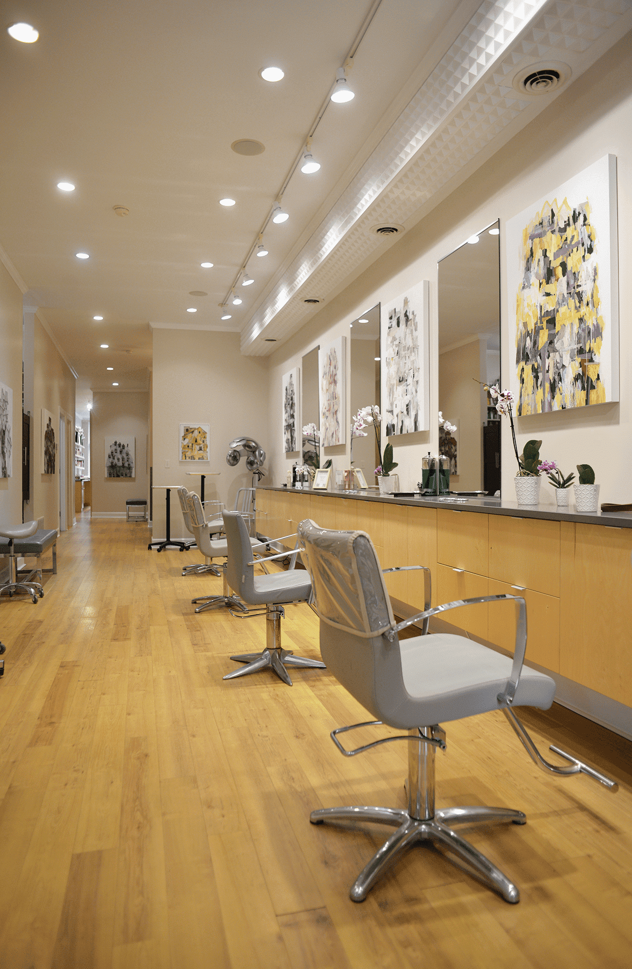 Modern hair salon interior with wooden floors, sleek chairs, and abstract art on walls.